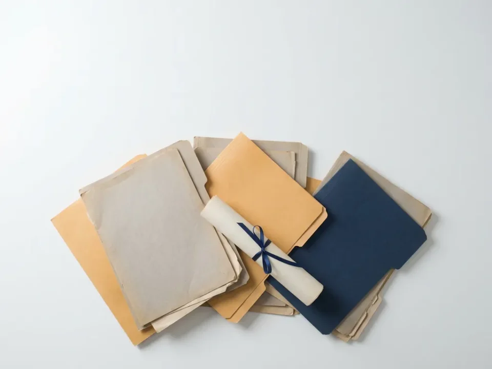 Loskomende stapel contractpapieren en arbeidsovereenkomsten op wit bureau, gefotografeerd van bovenaf in warme grijze en amberkleurige tinten.