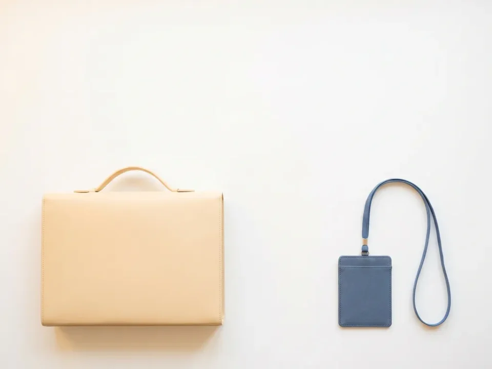 Minimalistische bovenaanzicht van een zelfstandige aktetas en een badge aan lanyard op wit bureau, symboliseert freelancer versus uitzendbureau.