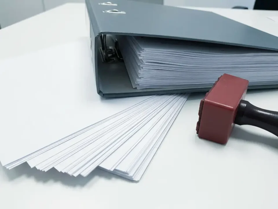 Open juridische documentenmap op wit bureau met rood administratief stempel en geordende papieren in grijze kantooromgeving.